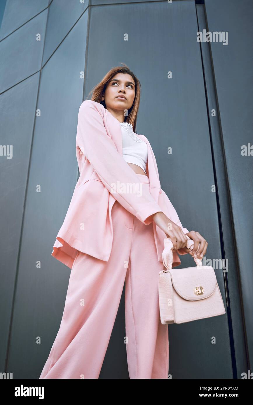 Young trendy and confident mixed race woman looking stylish while posing and chilling time in the city. Fashionable hispanic woman wearing pink clothes and a handbag, ready for an interview downtown Stock Photo