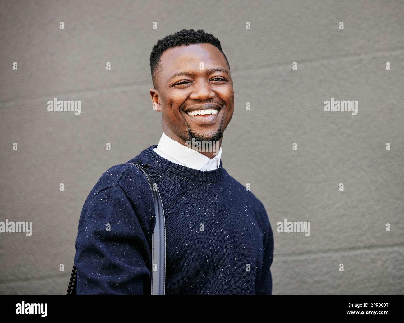 Portrait of a young businessman standing in the street in the city smiling and looking happy on a sunny day. African american male expressing happiness on his face Stock Photo
