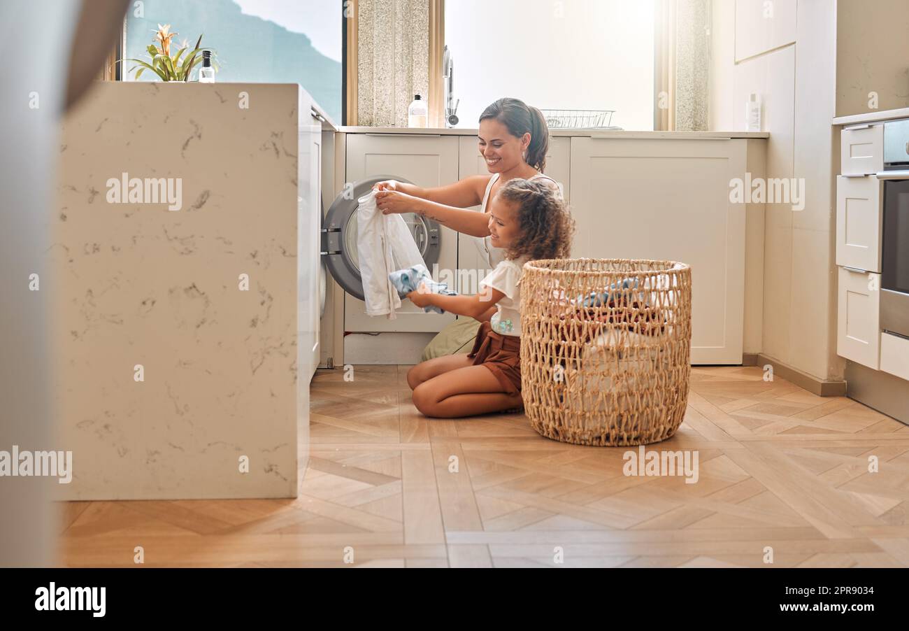 Young hispanic mother and her daughter sorting dirty laundry in the washing machine at home. Adorable little girl and her mother doing chores together at home Stock Photo