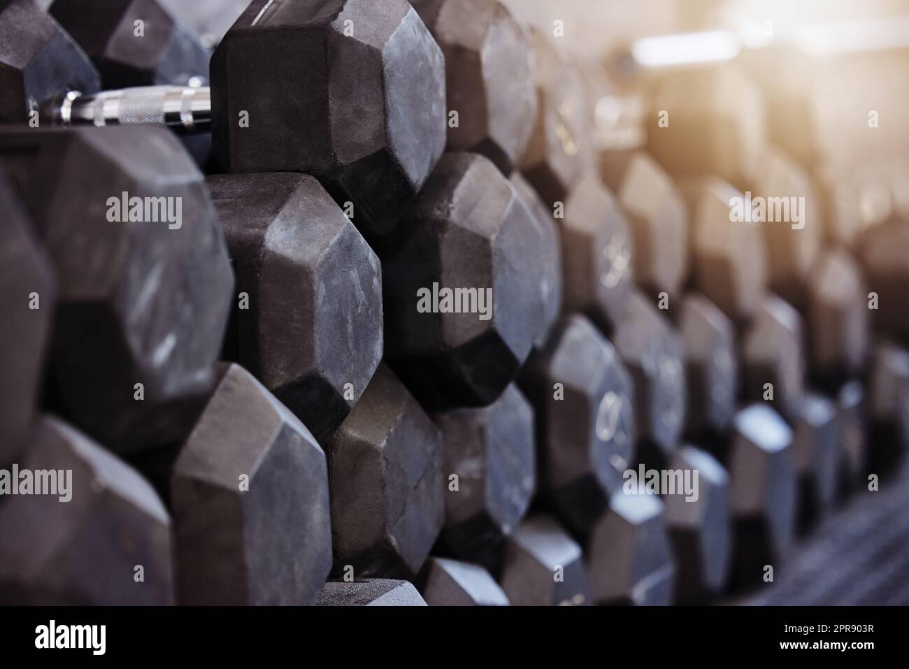 Closeup of stacked and piled heavy dumbbell weights arranged in empty gym with nobody during day. Weightlifting equipment organised in groups in health and sports centre with no one. Healthy routine Stock Photo