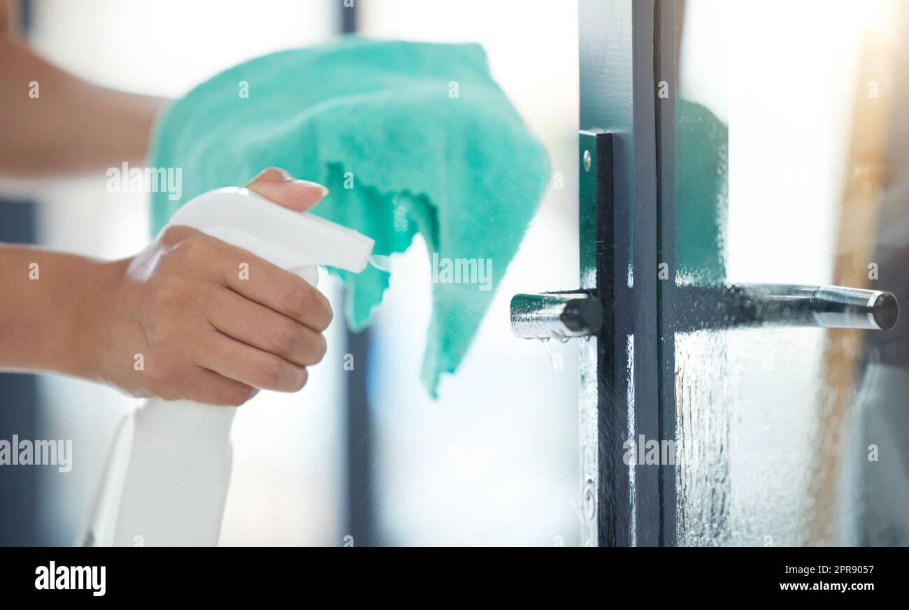 One unknown mixed race domestic worker using a cleaning product on a door handle. An unrecognizable woman enjoying doing chores in her apartment Stock Photo