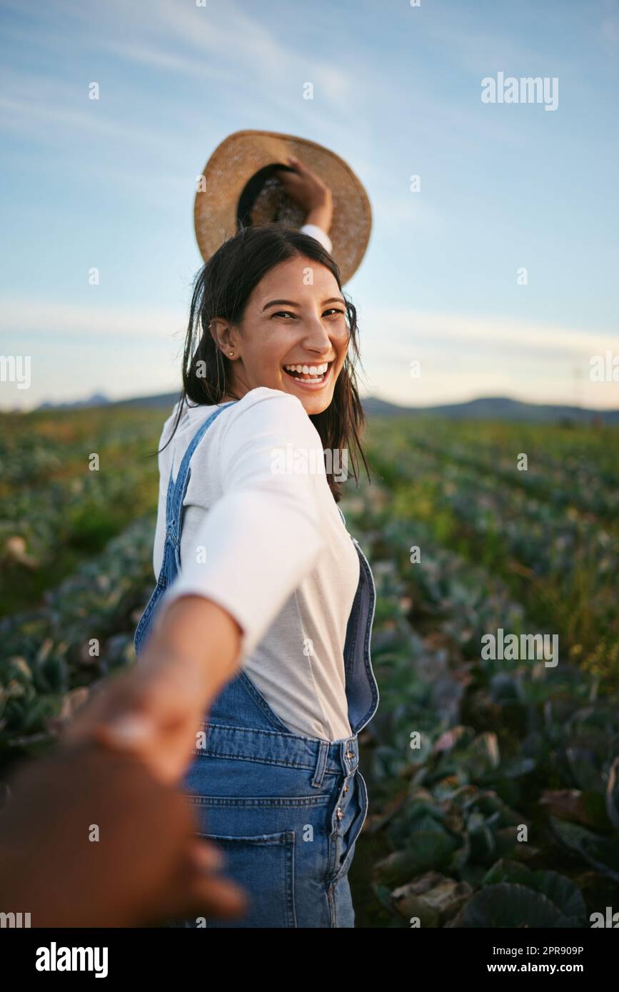 Portrait of a woman in farmer attire holding the hand of her boyfriend while walking in a cabbage field. Unrecognisable person holding hands with a brunette woman on a romantic walk on a farm Stock Photo