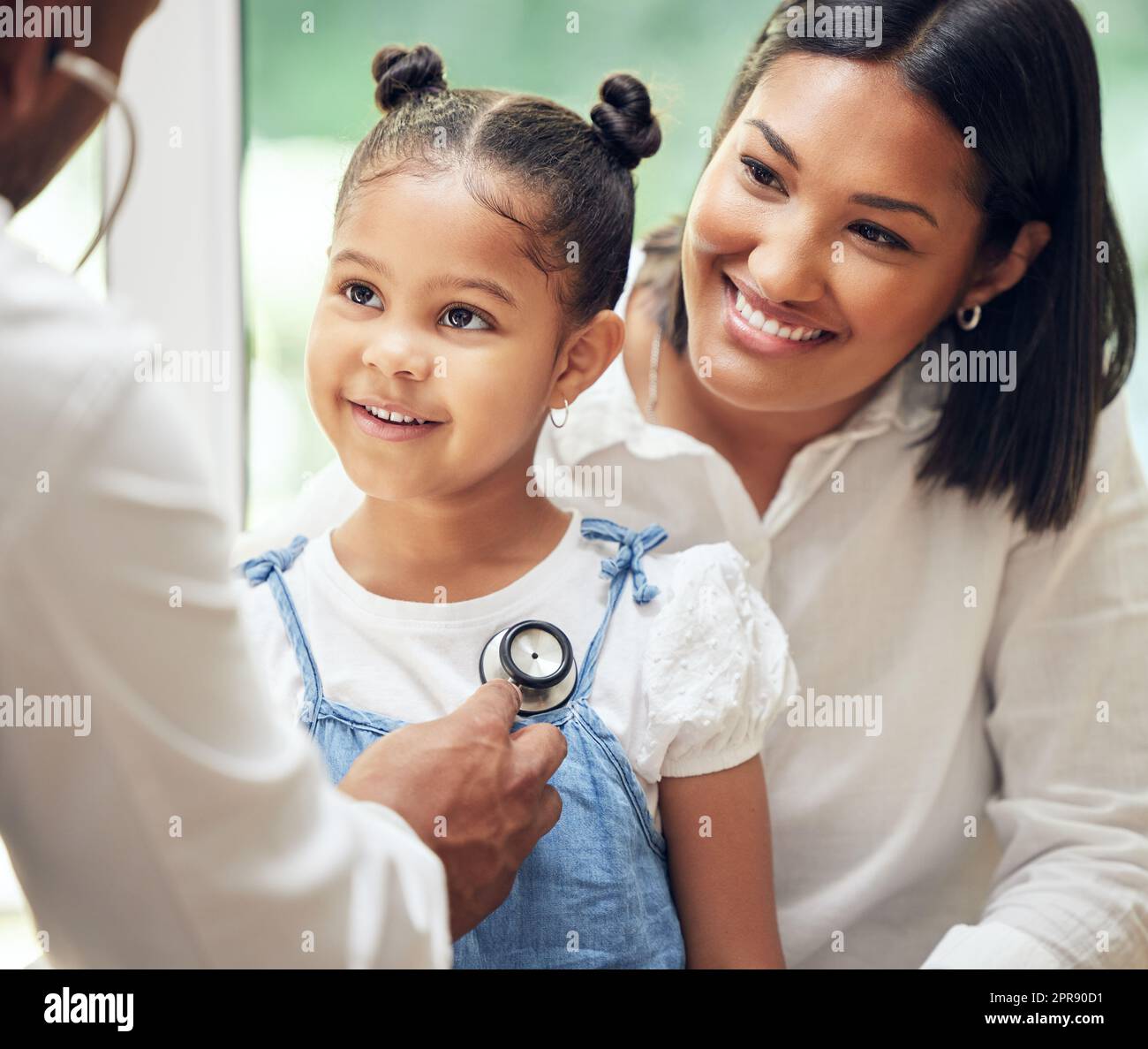 Doctor examining happy little girl by stethoscope. Child sitting with