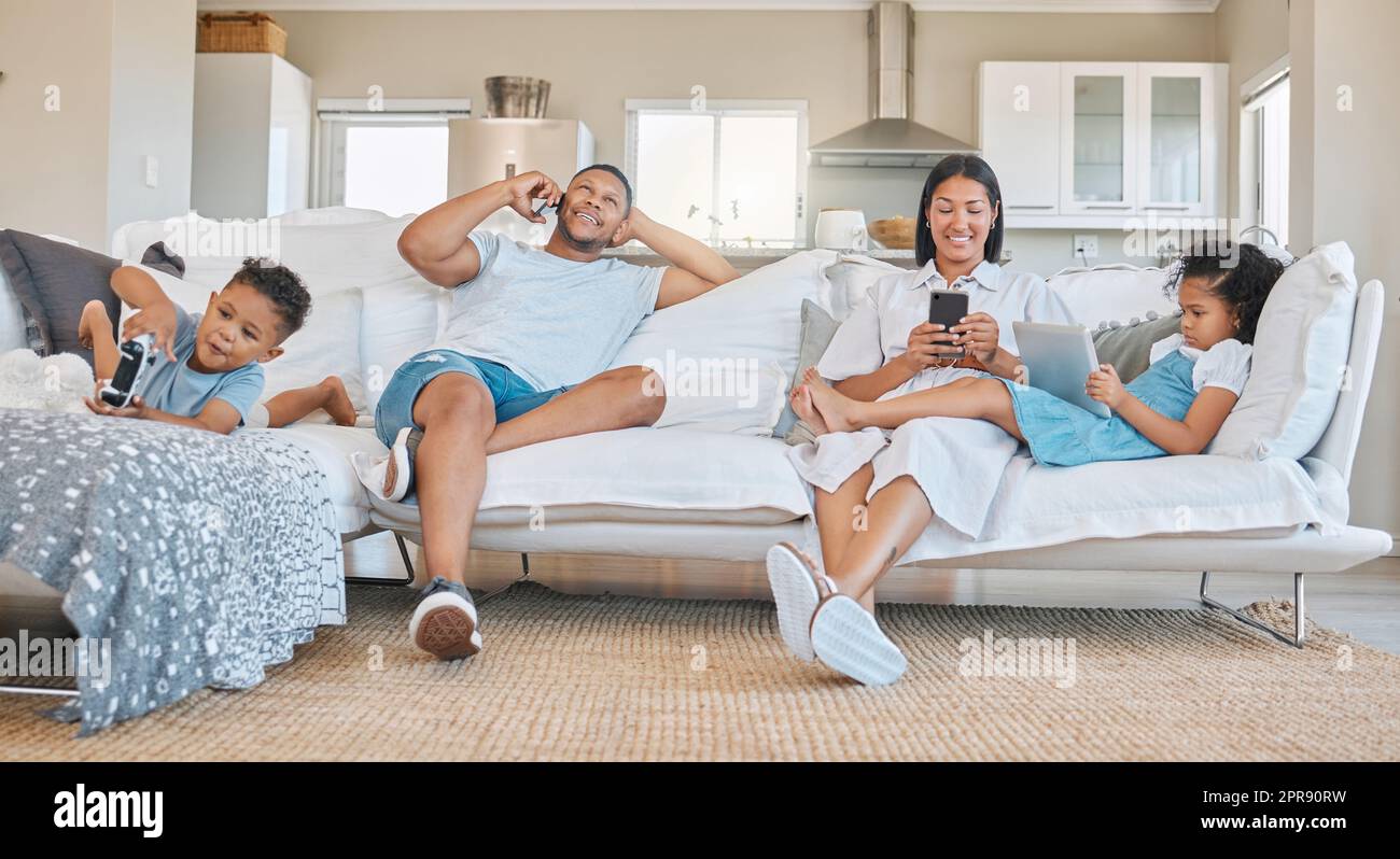 We all chill differently. a young family sitting together using different devices. Stock Photo
