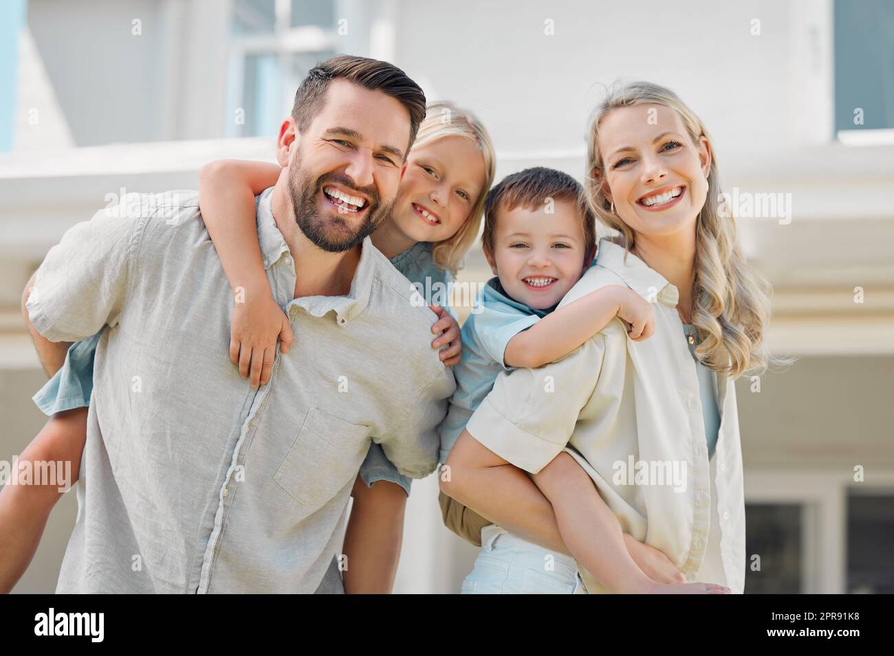 Portrait of happy parents giving their little children piggyback rides outside in a garden. Smiling caucasian couple bonding with their adorable son and daughter in the backyard. Playful kids enjoying Stock Photo