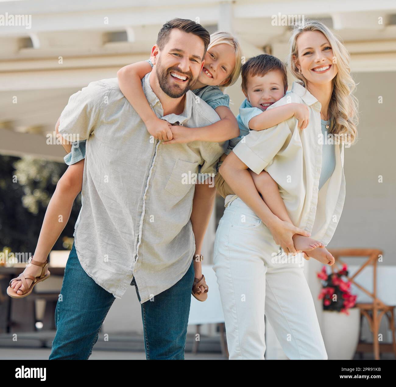 Portrait of happy parents giving their little children piggyback rides outside in a garden. Smiling caucasian couple bonding with their adorable son and daughter in the backyard. Playful kids enjoying Stock Photo