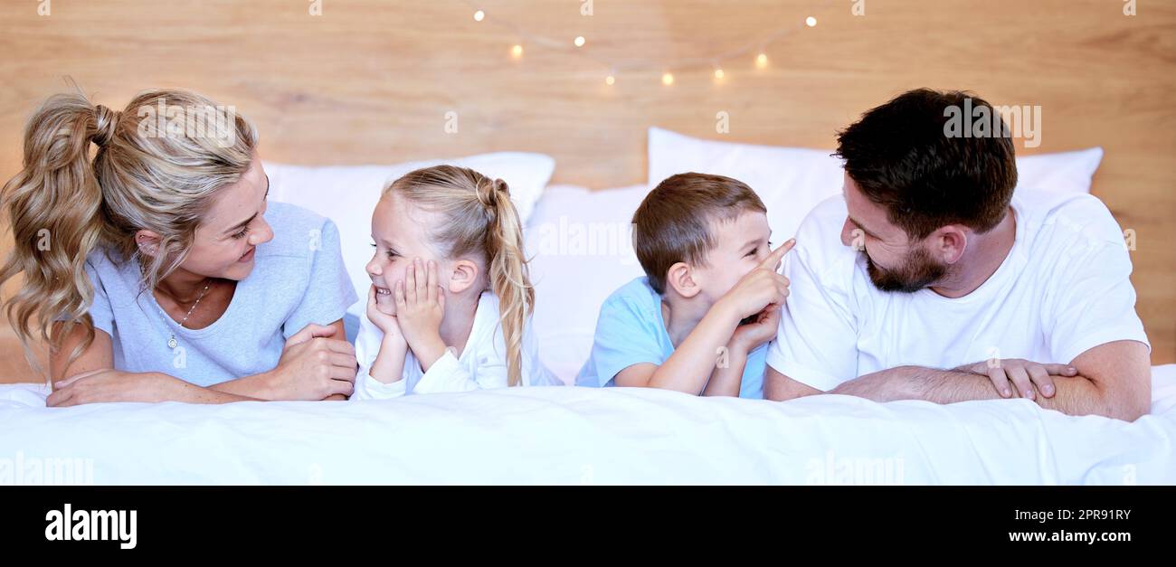 Happy carefree caucasian family lying cosy on bed while bonding together at home. Loving parents spending quality time with little son and daughter. Cute kids enjoying lazy morning with mom and dad Stock Photo