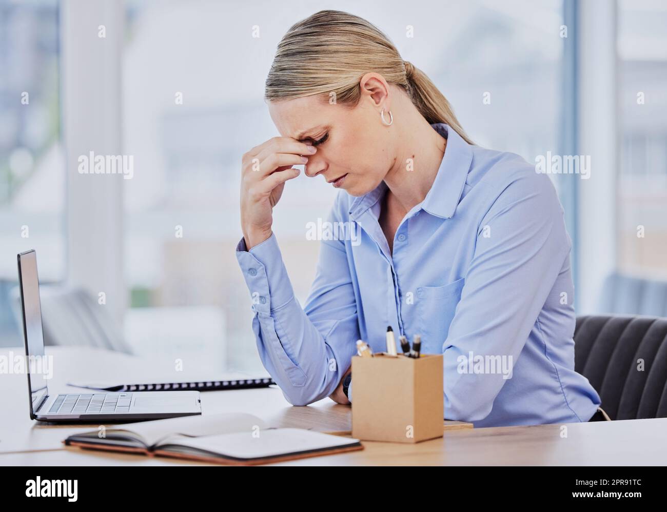 Young frustrated caucasian business woman working at office desk suffering from chronic headaches while sitting in front of laptop. Female professional looking stressed and overworked Stock Photo