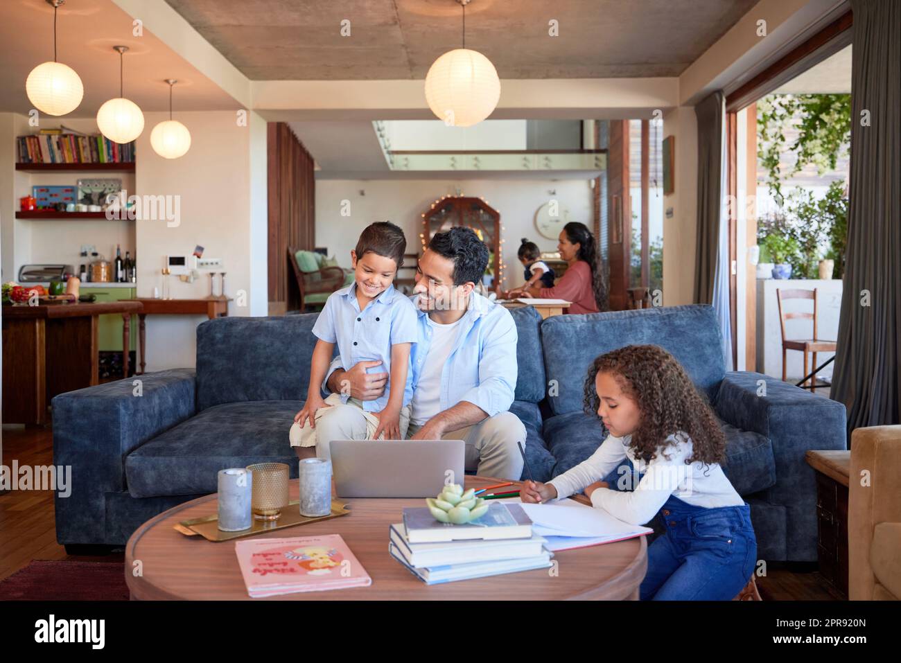 Father using a laptop at home with children. A happy dad online with his a and daughter. Young mixed race man with a little boy and girl using a computer, doing homework, learning and working remote Stock Photo