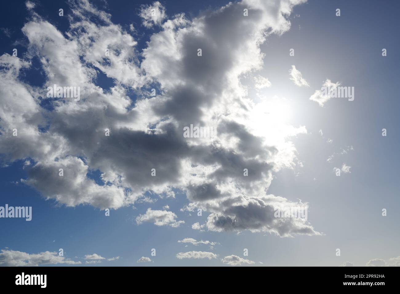 Clouds. Sun hiding behind clouds with blue sky. Beautiful sunshine from behind white and grey cumulus clouds at midday in summer. Serene view of natures outdoor beauty high in space. Stock Photo