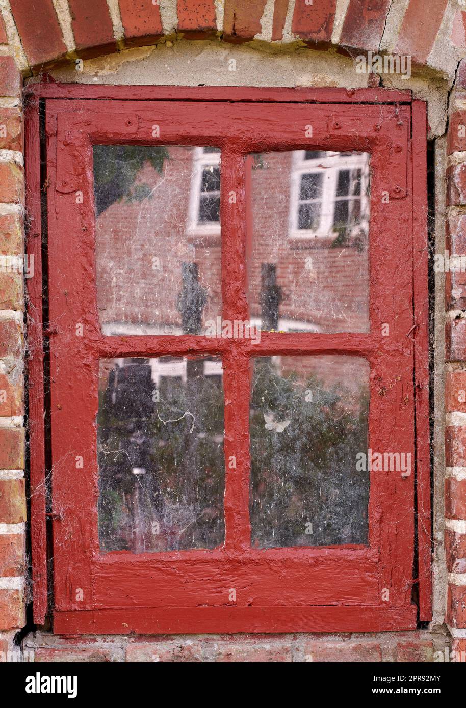 Closeup of an old dirty window in a red brick home. Zoom in on casement with red wood frame on a historic building with bumpy paint texture. Macro exterior details of windowsill in a traditional town Stock Photo