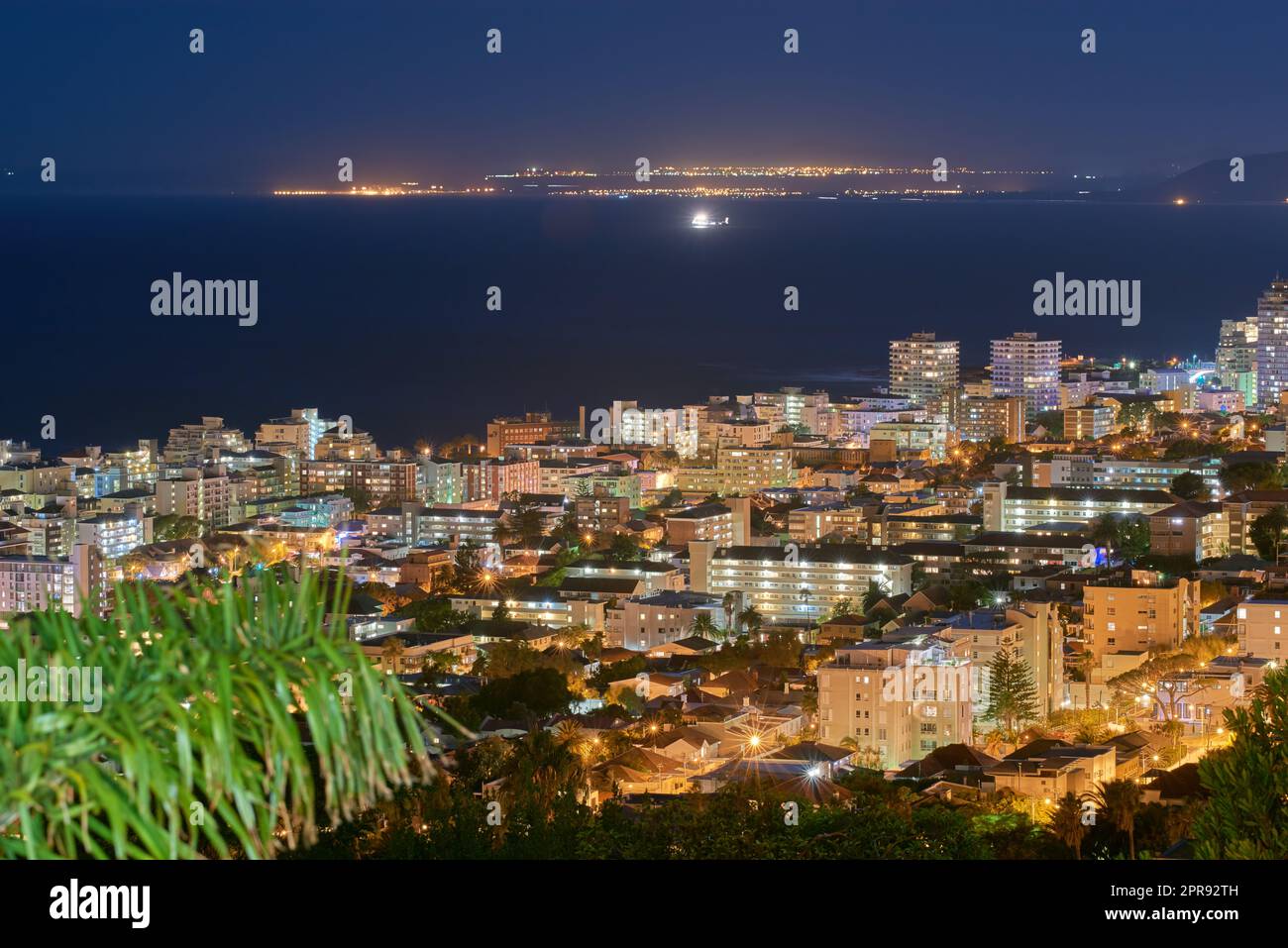 Urban city lights against a midnight sky with copy space. Skyline with colorful lighting and the open ocean on the horizon. Modern architectural buildings, vacation hotels in an urban city Stock Photo