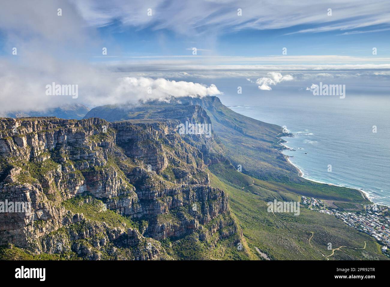 Aerial view of mountain and calm ocean with a blue cloudy sky background and copy space. Stunning nature landscape of the sea and horizon from Table Mountain with beautiful greenery in Cape Town Stock Photo