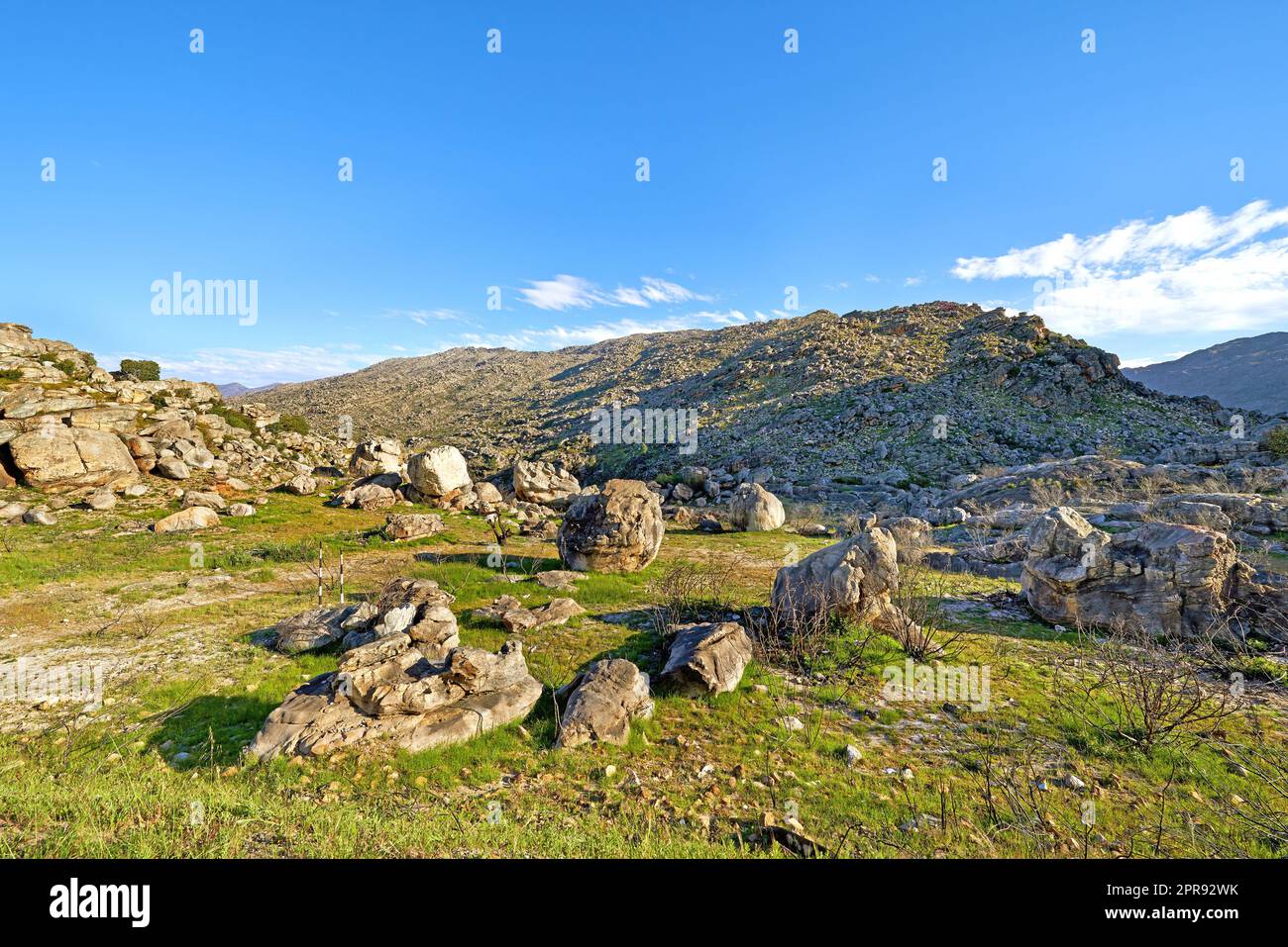 A rocky mountainside landscape with green lush grass growing in an ecological rural environment. Beautiful field on rough terrain in nature with a scenic blue sky in the Western Cape during summer Stock Photo