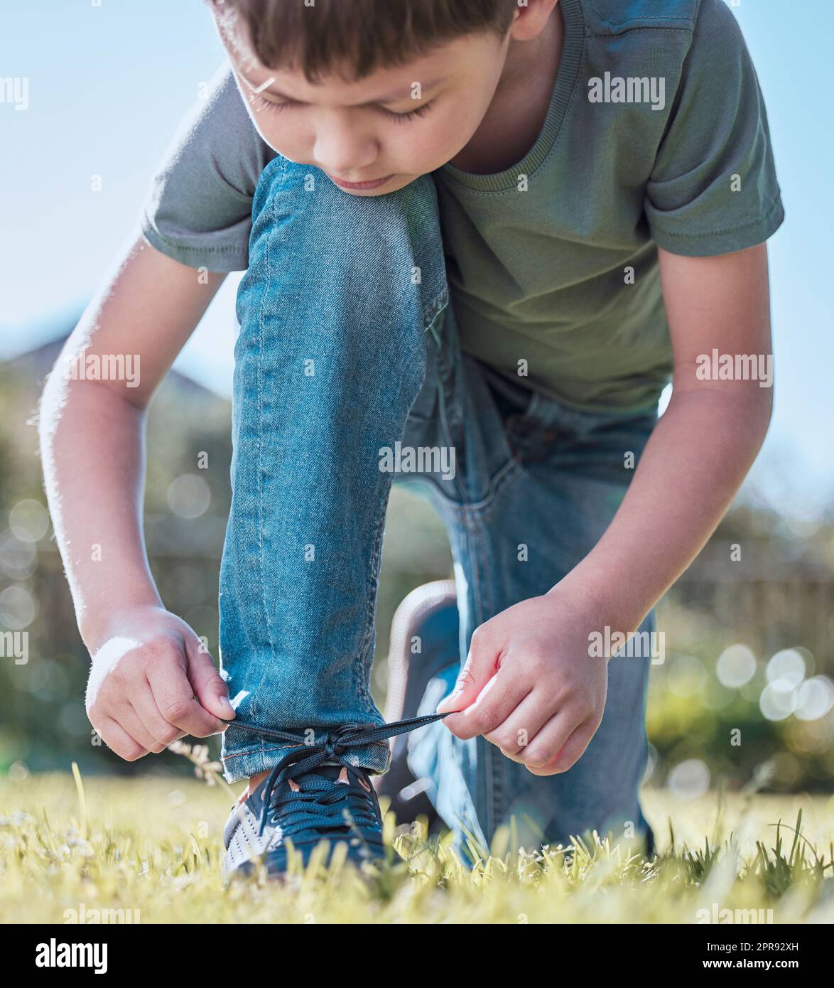 I can tie my own laces, whats next. an adorable little boy tying his shoelaces outside. Stock Photo