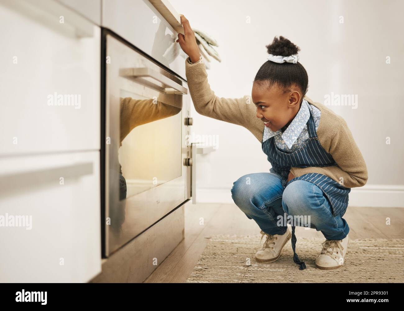 How much longer. a little girl watching her baked goods cook in the oven at home. Stock Photo