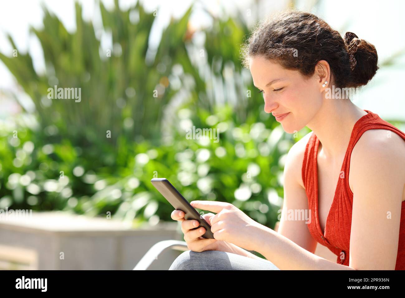 Woman using smart phone sitting on bench in a park Stock Photo