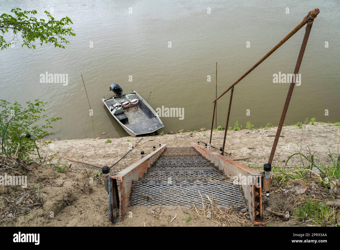 steep metal stairway leading down to water and a fishing boat on a shore of the Missouri River at Lupus, MO Stock Photo