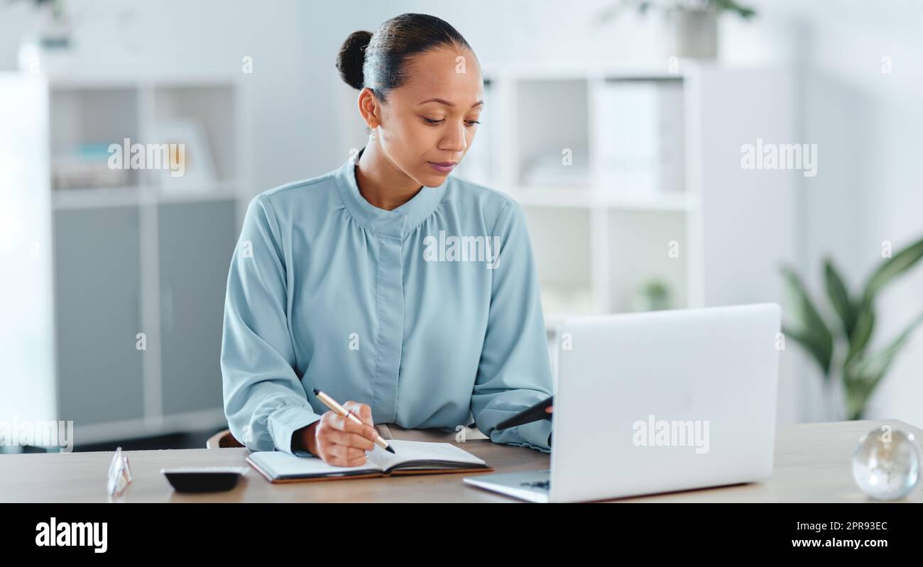 Busy, smart and serious business manager with a laptop working on schedule, planning and brainstorming ideas inside office. Lady marketing analyst writing strategy for project plan in her diary Stock Photo
