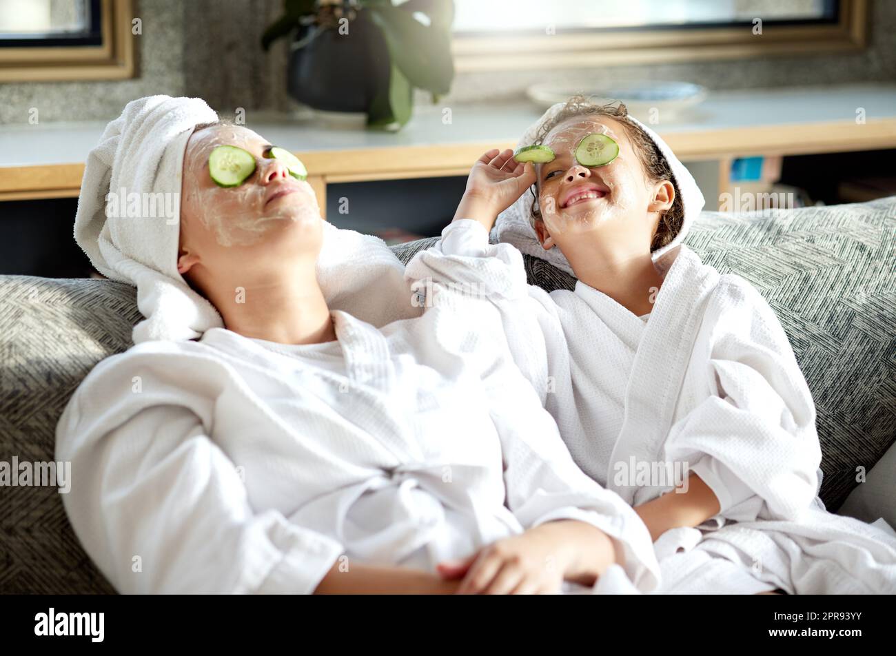 Fresh skincare, face mask and healthy skin treatment for bonding mother and daughter home spa day. Fun, smiling and playful child and parent relaxing with cucumber over their eyes in grooming routine Stock Photo