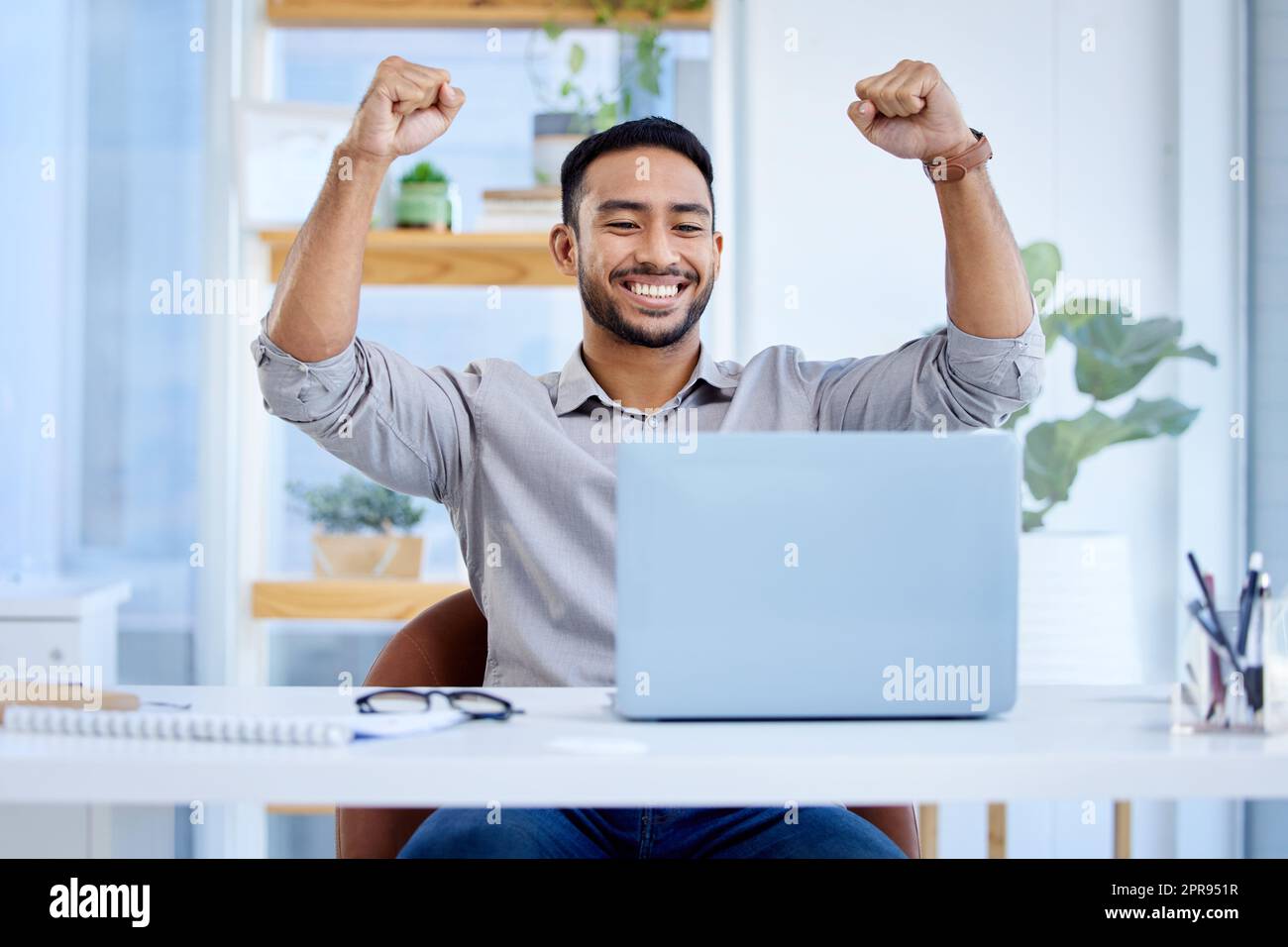 This win will be big for my business. a young businessman cheering while working on a laptop in an office. Stock Photo