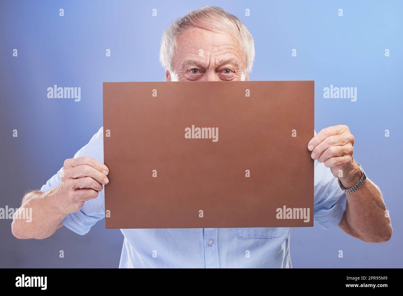But you didnt hear it from me... Studio shot of a senior man holding a blank sign against a blue background. Stock Photo