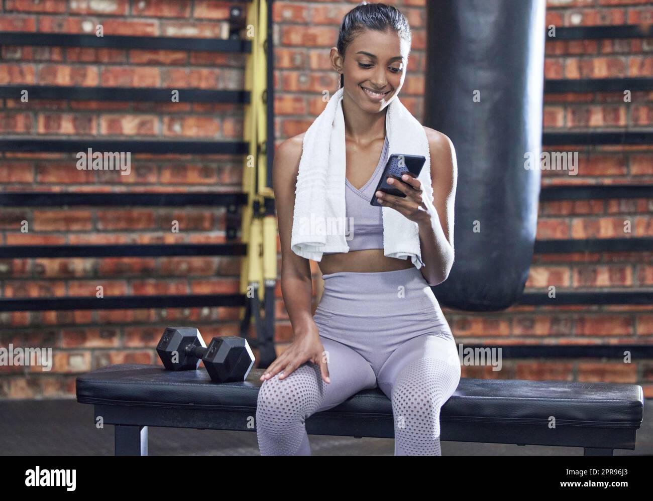 Lets see on my fitness app if I reached my goals. a sporty young woman using a cellphone while taking a break in a gym. Stock Photo