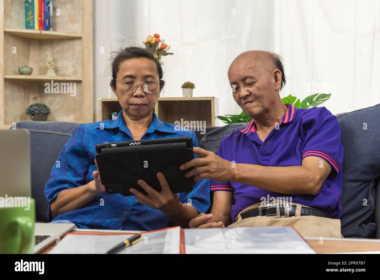 Elderly Asians use tablets and insurance documents at home. Stock Photo