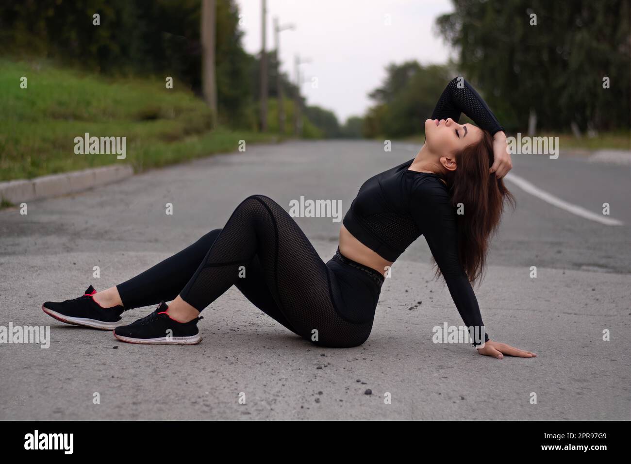 A girl on the road in a black sports tight suit. Stock Photo