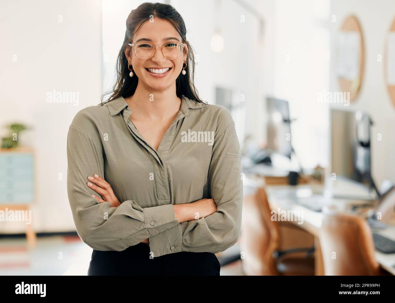 Im more confident in my workplace. an attractive young businesswoman standing alone in the office with her arms folded. Stock Photo