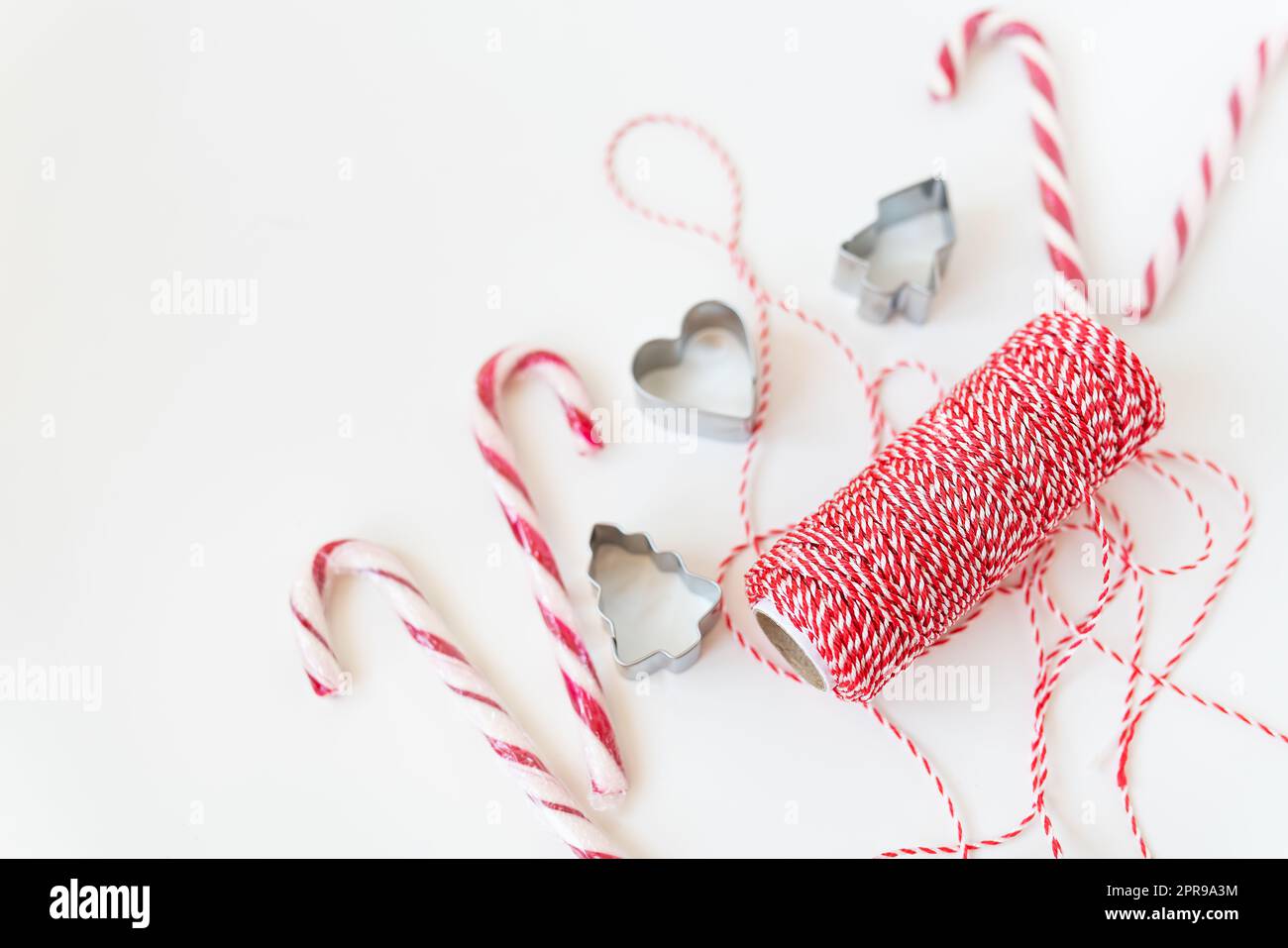 Christmas candies, along with cookie cutters, red thread for wrapping gifts, lie on a white table. Christmas and New Year's Eve 2023-2024. Stock Photo