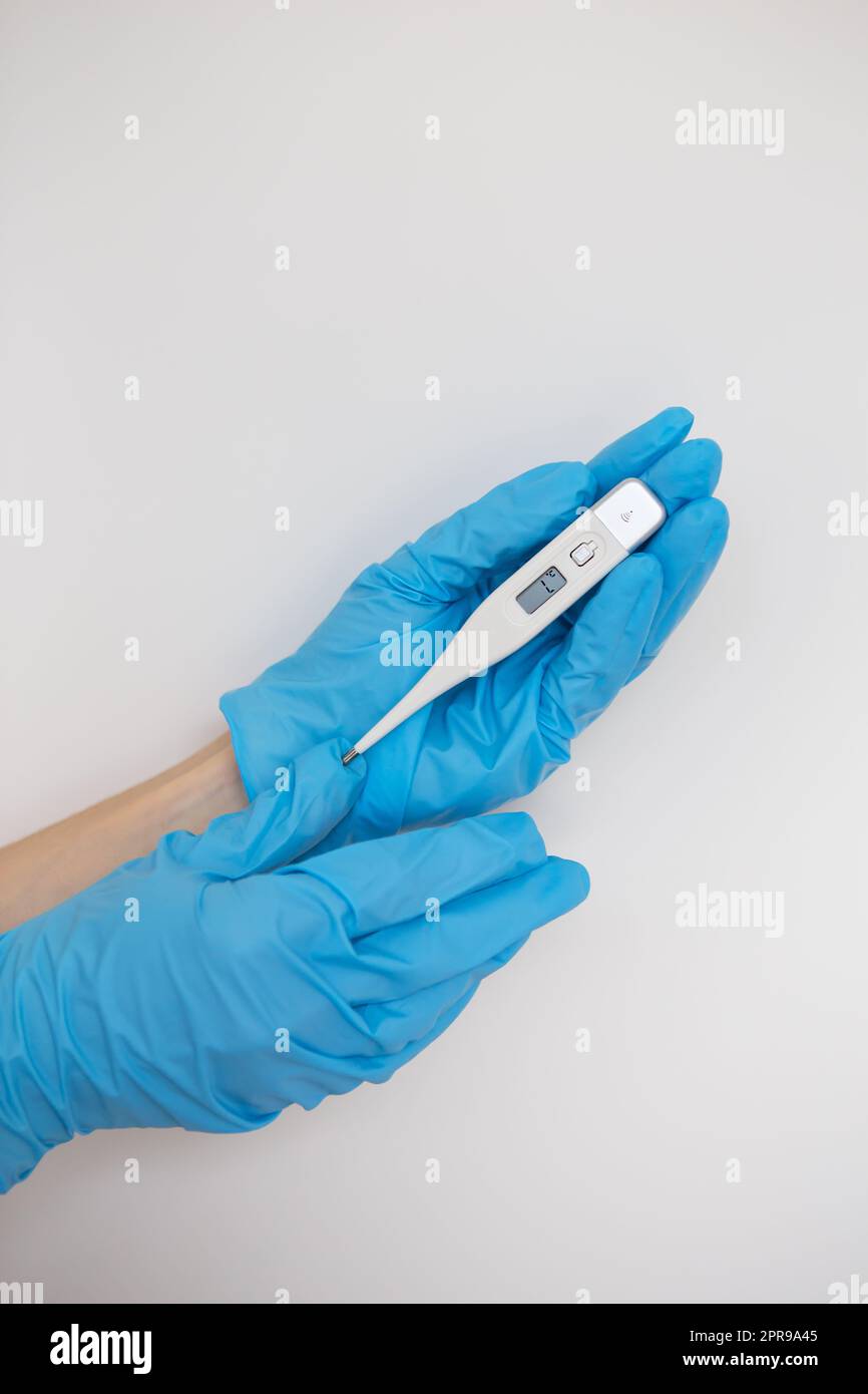 Medic's hand wearing a blue latex glove holding a thermometer Stock Photo