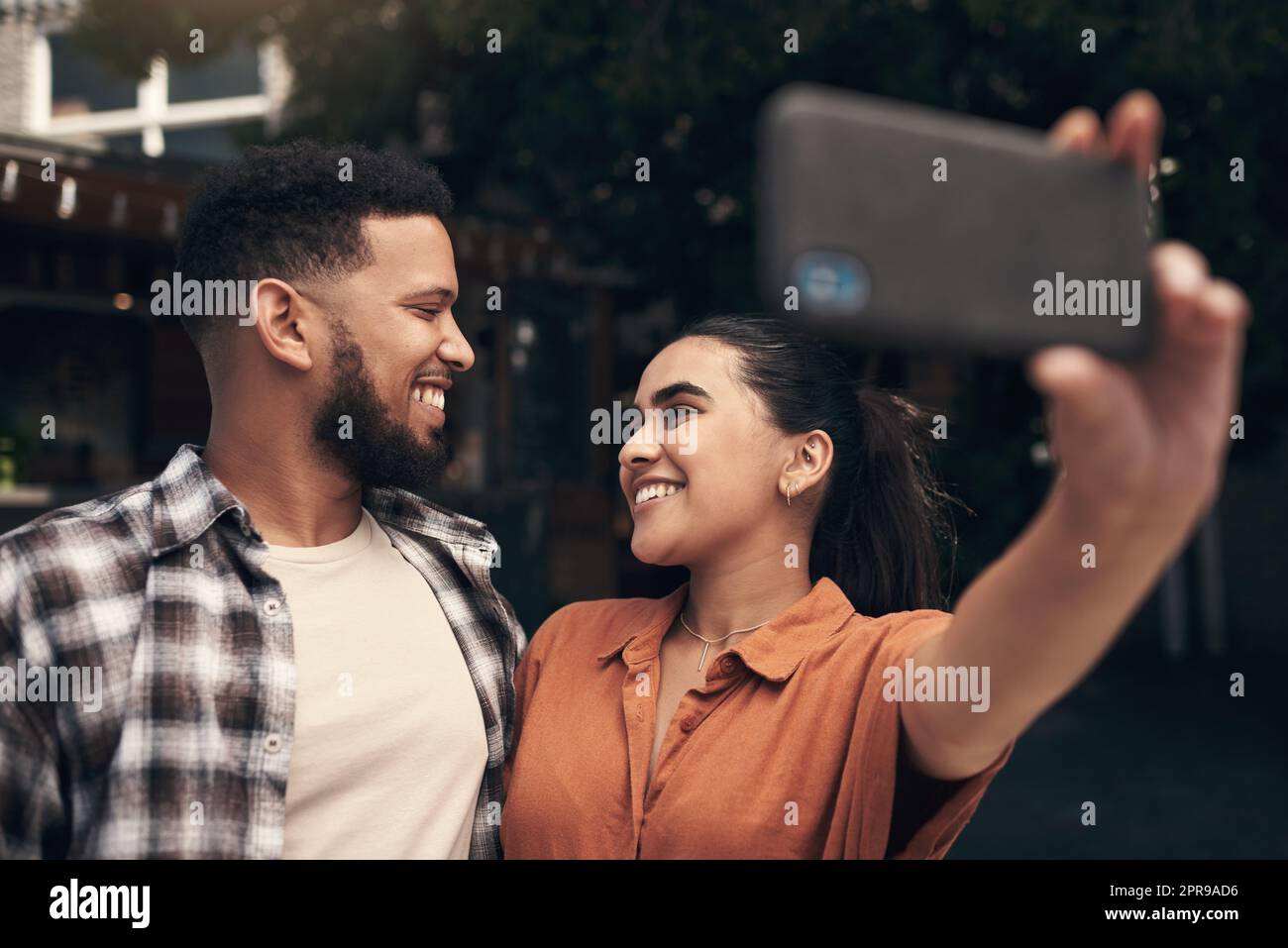 We have to capture the perfect day out. two young friends standing outside a restaurant and using a cellphone to take a selfie. Stock Photo