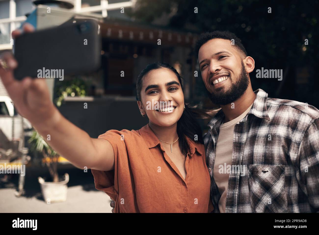 Some much needed bonding time. two young friends standing outside a restaurant and using a cellphone to take a selfie. Stock Photo