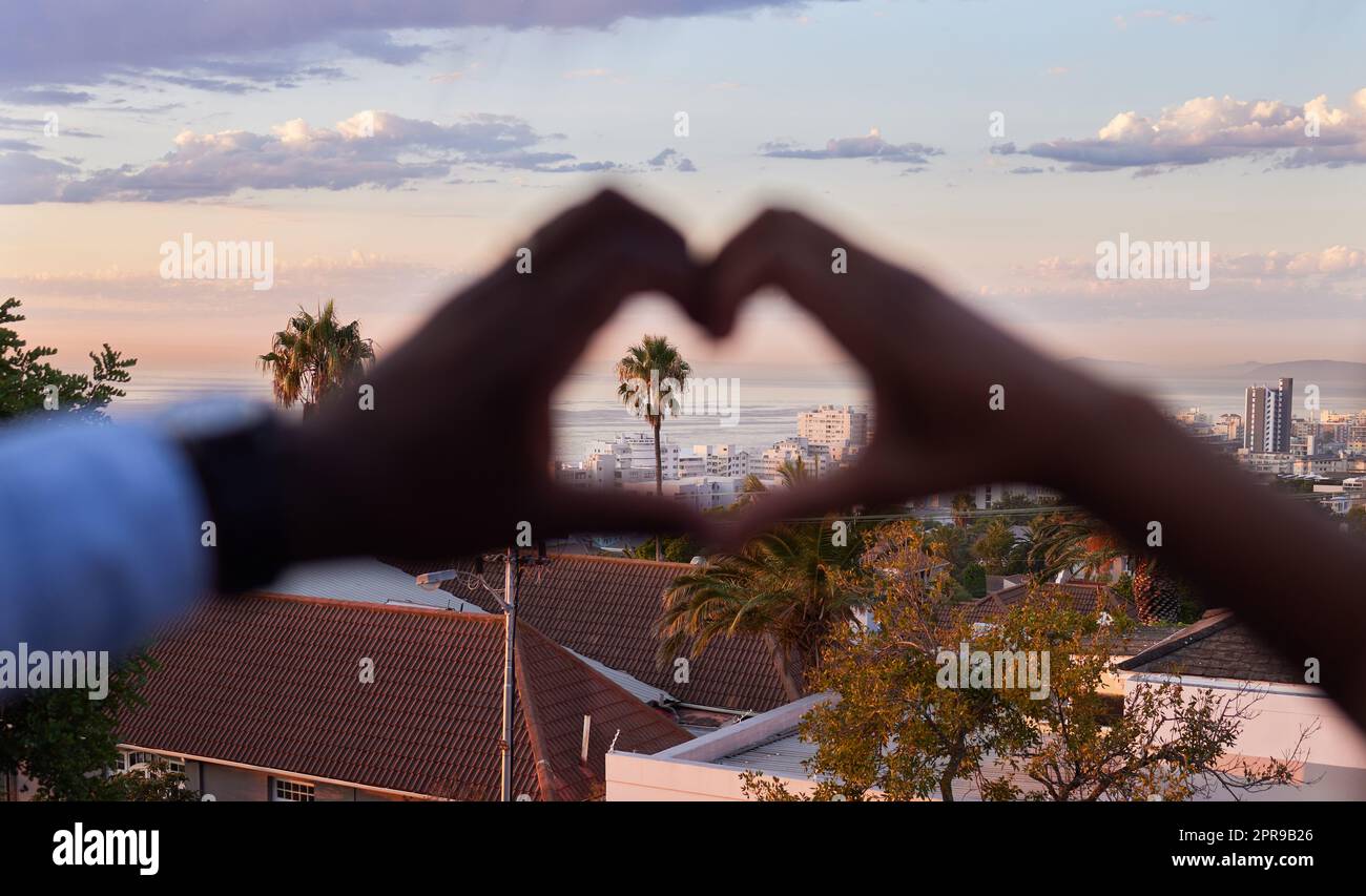 Living a life full of love. an unrecognizable couple making a heart shaped gesture with the city in the background. Stock Photo