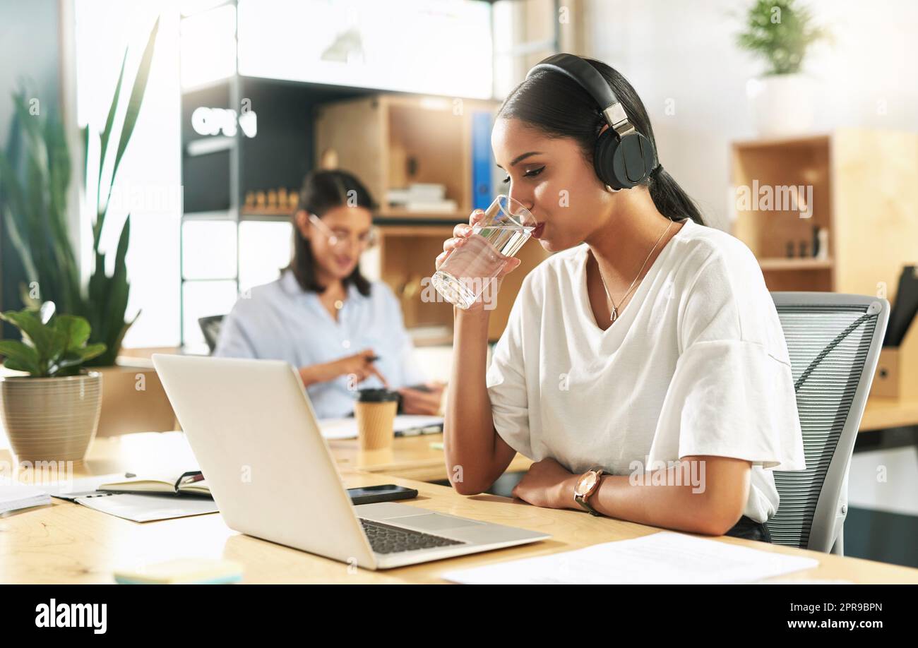 Its important to keep hydrated. a young businesswoman drinking a glass of water at work Stock