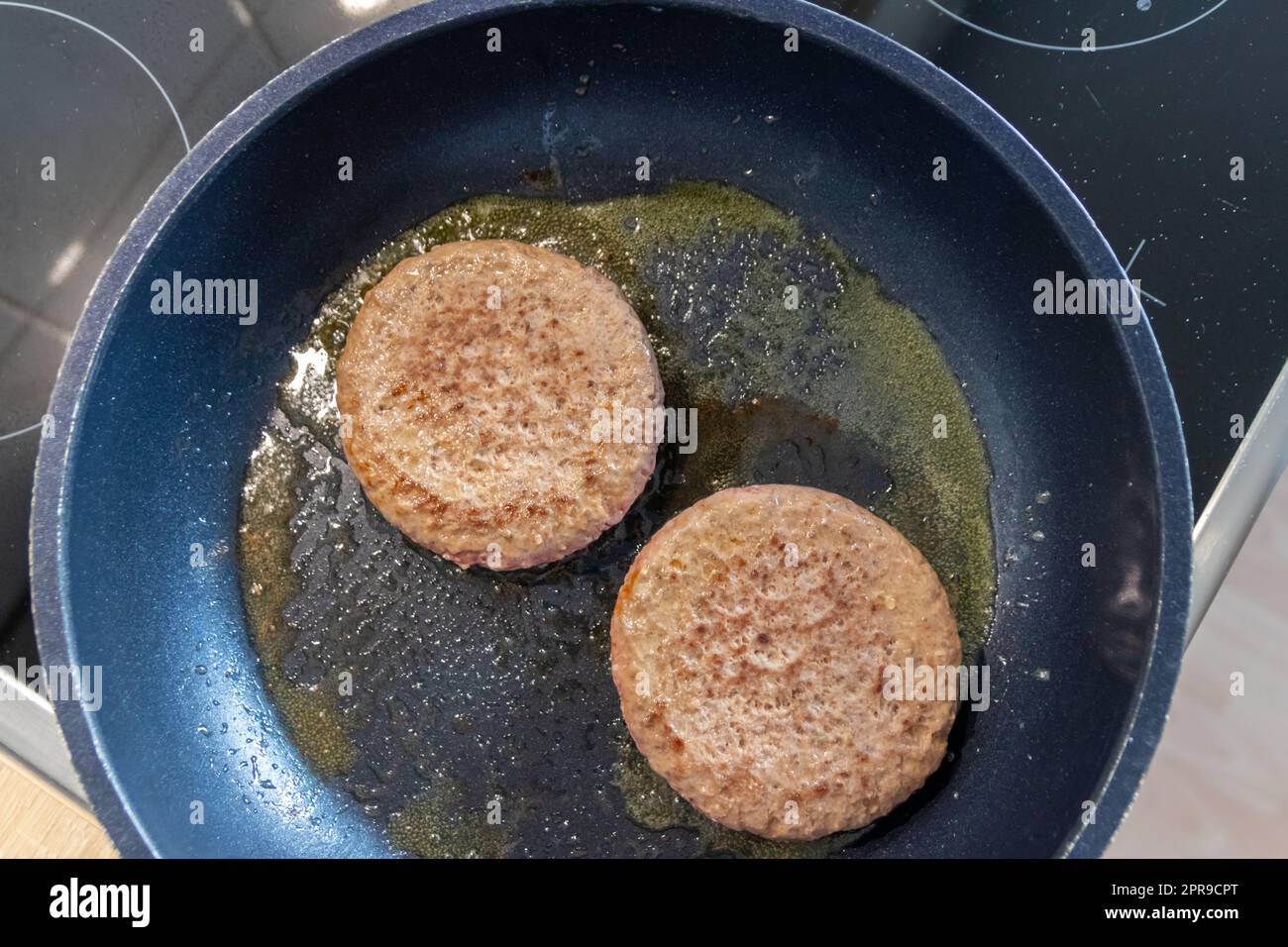 Two burger patties burger meat sizzling in hot pan with fat and oil as