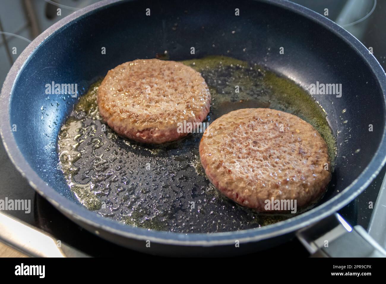 Two burger patties burger meat sizzling in hot pan with fat and oil as