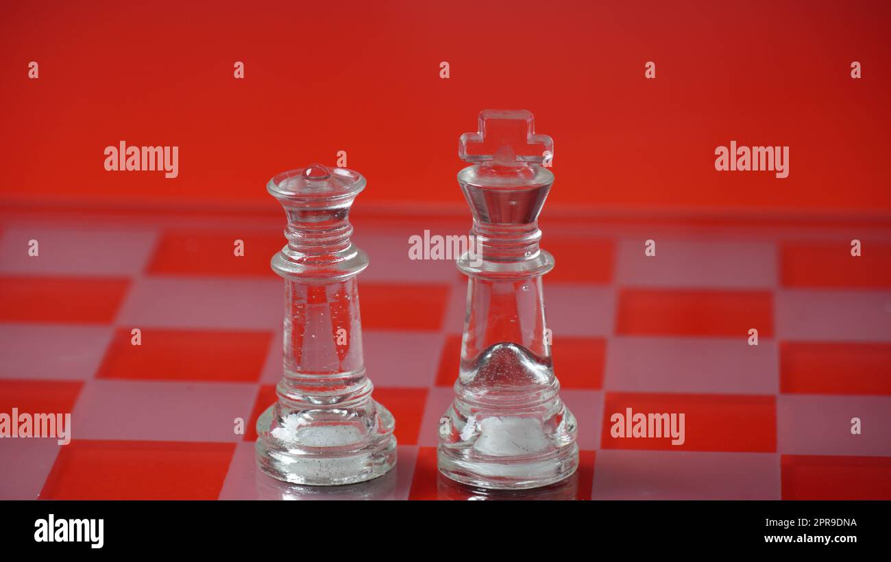 Pieces of transparent chess, king and queen. Transparent chess figures on chessboard, red tone. Stock Photo