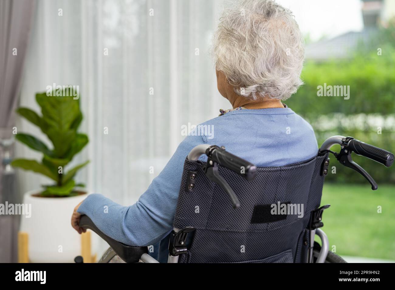 An elderly woman sitting on wheelchair looking out the window for waiting someone. Sadly, melancholy and depressed. Stock Photo