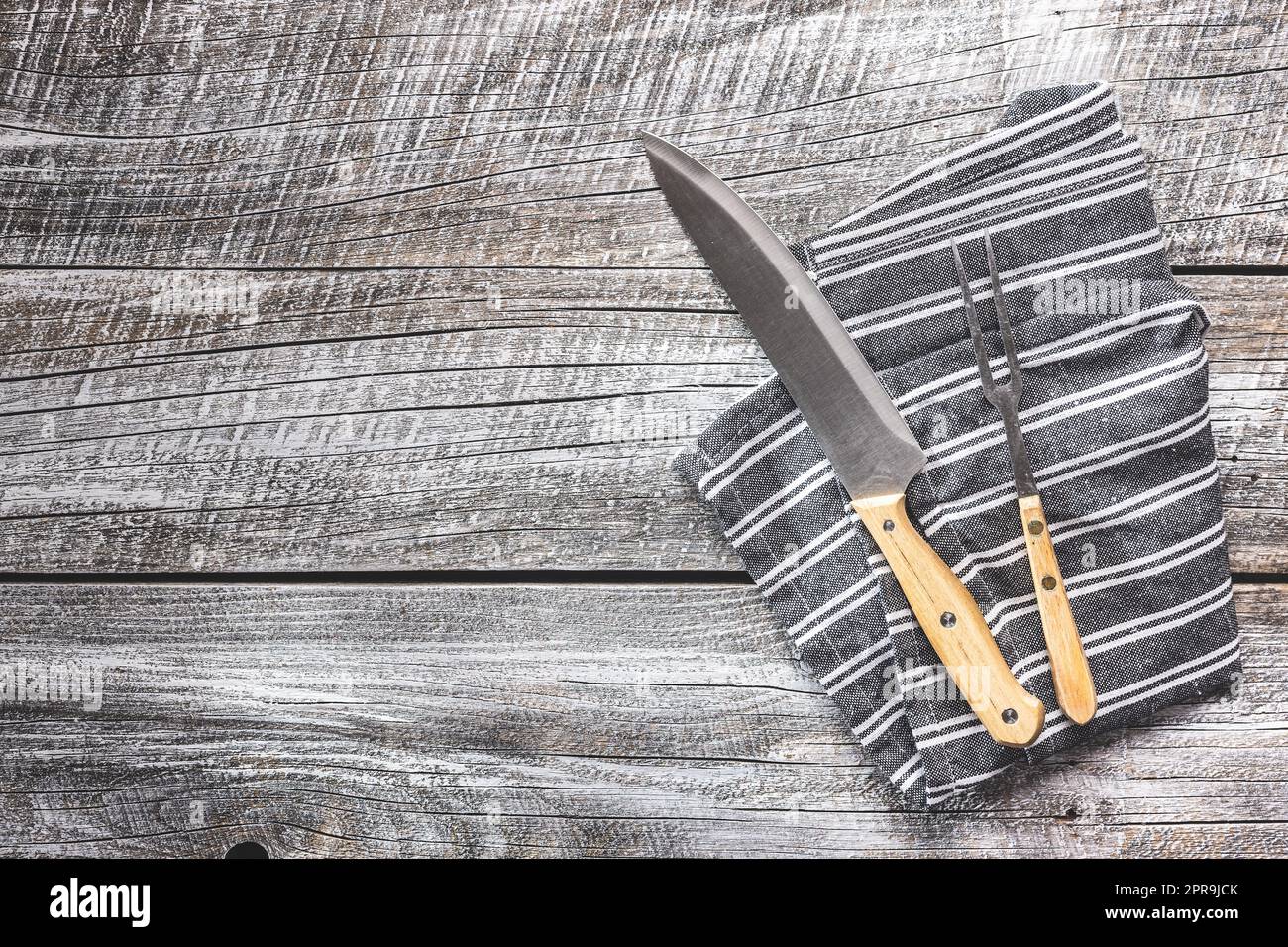 Knife and fork on napkin on wooden table. Stock Photo