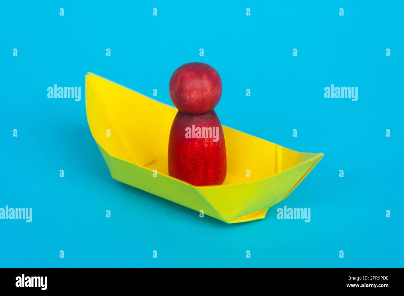 Red wooden figure on yellow paper ship with blue background. Stock Photo