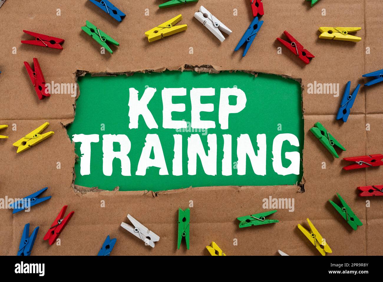 Text caption presenting Keep Training. Business approach Grounding Drilling Always Wonder Be Curious Learn Important Ideas Written Under Ripped Cardboard With Colored Pegs Around. Stock Photo