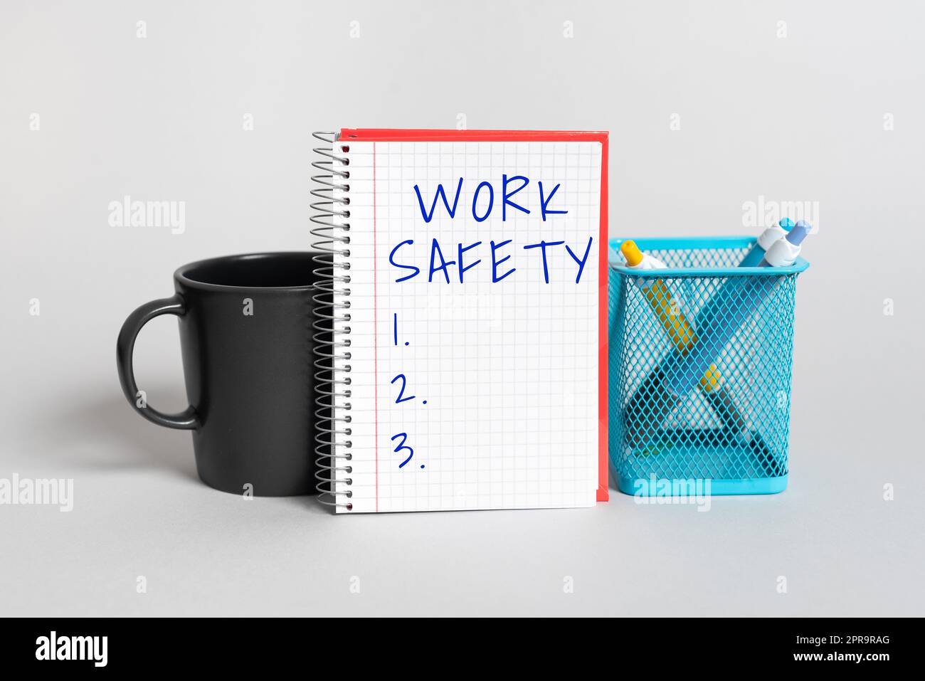 Conceptual display Work Safety. Word for Policies and control in place according to government standard Cup, Notebook With Important Message And Pencil Case On Desk Stock Photo