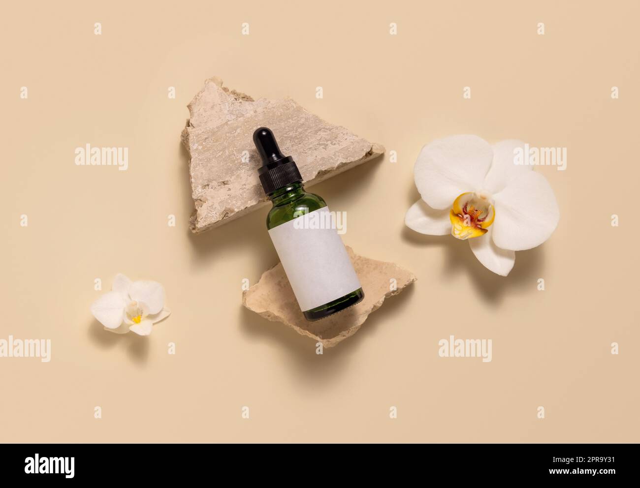 Green glass dropper bottle on stones near white orchid flowers on light yellow, Mockup Stock Photo