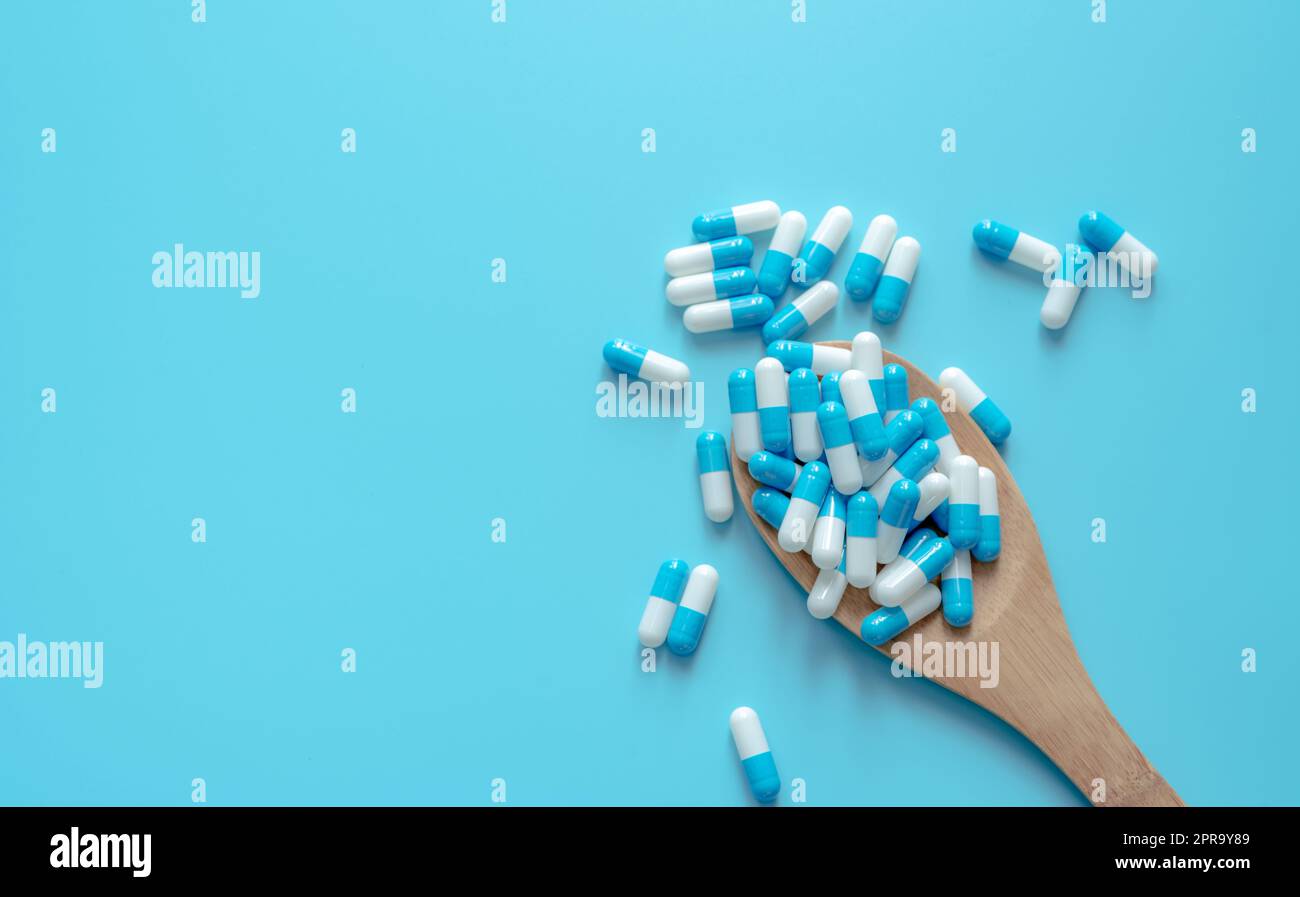 Blue-white capsule pills on wooden spoon. Capsule pills on blue background. Health topics. Drug for treatment illness. Medication use. Medical care. Pharmaceutical industry. Capsule pill production. Stock Photo