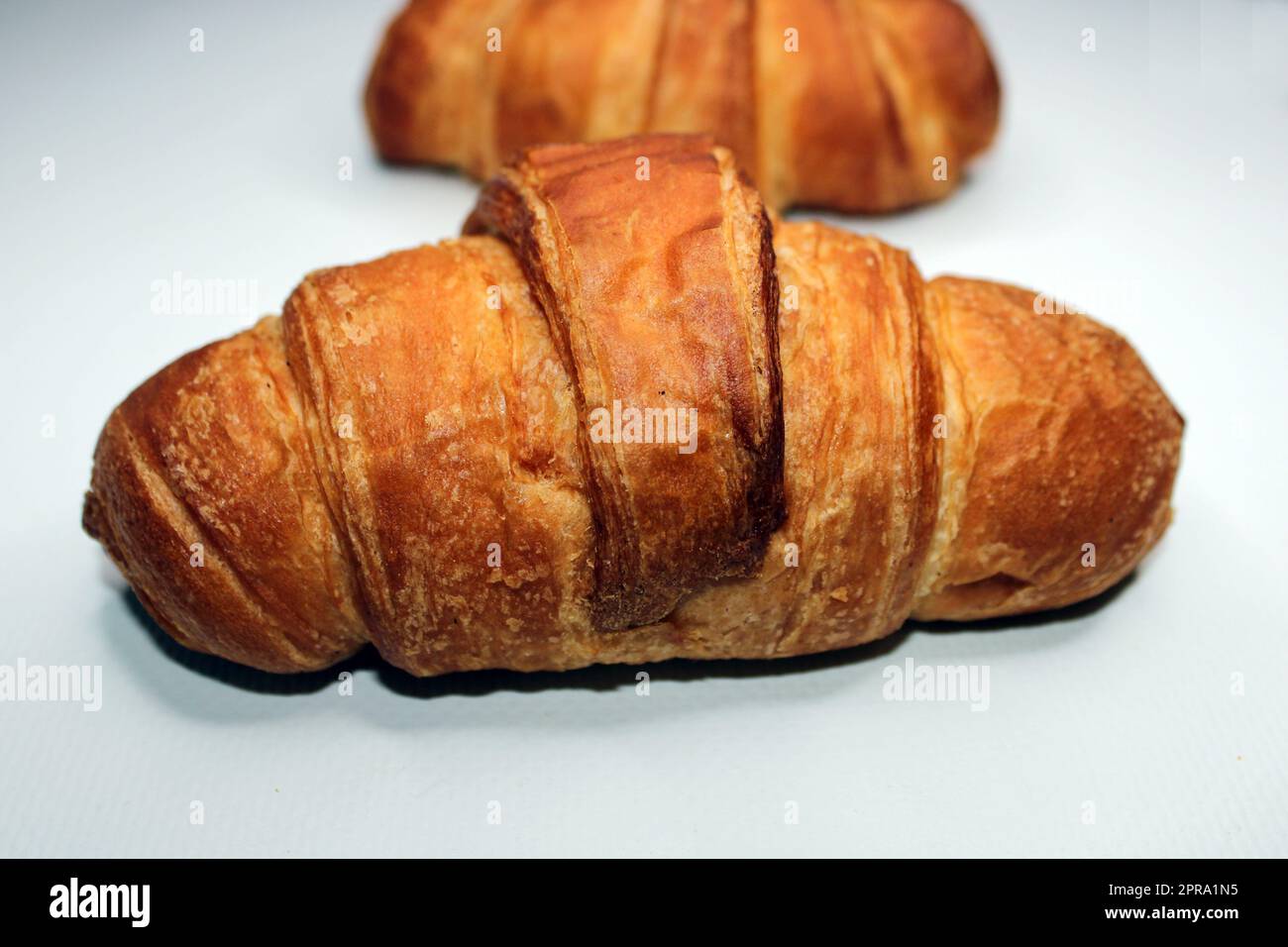 Fresh crispy croissant close-up on a light background. Blurred croissant in the background. Cooking, home baking Stock Photo