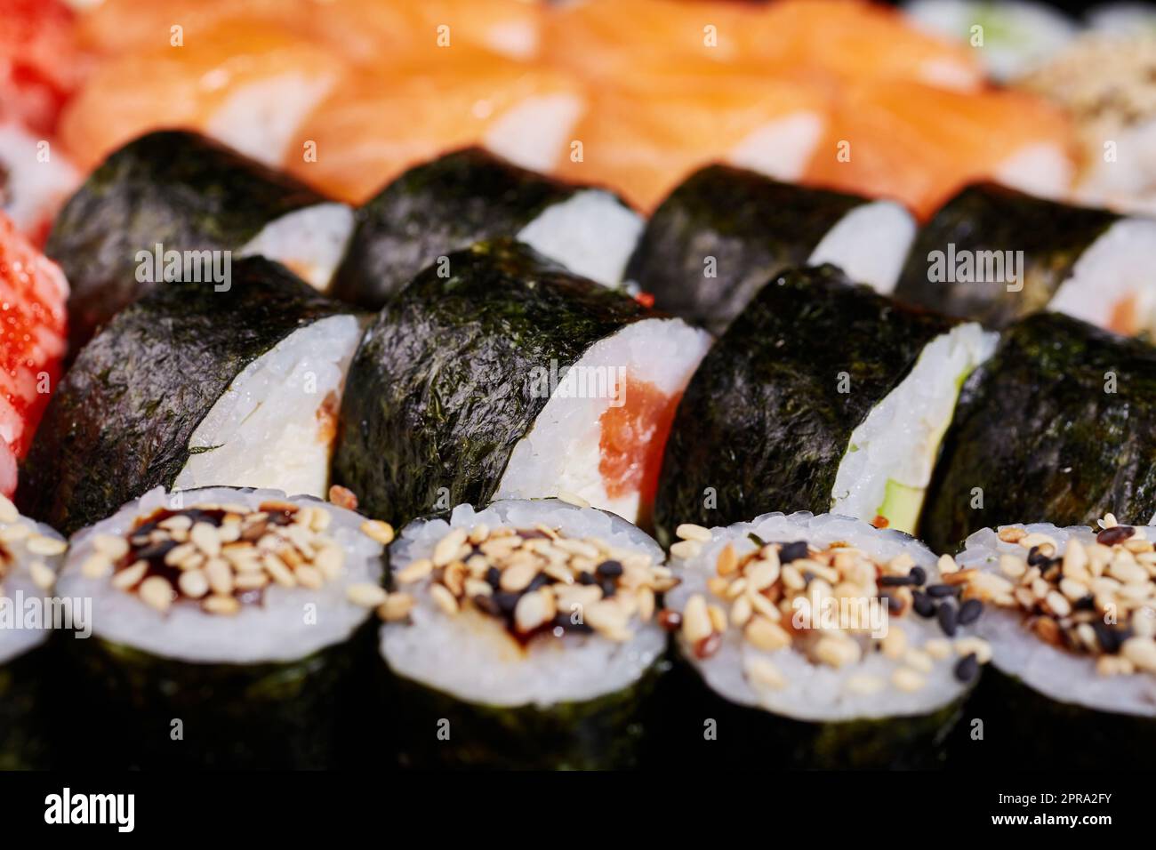 Close up of roll with salmon and sesame seeds wrapped in nori leaves. Stock Photo
