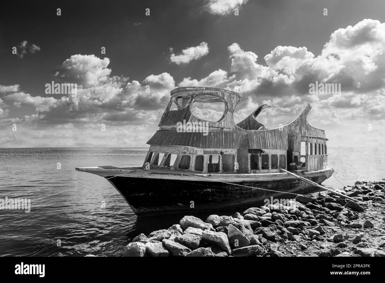 Old ship near stony shore floating in sea water near rocky coast against cloudy sky Stock Photo