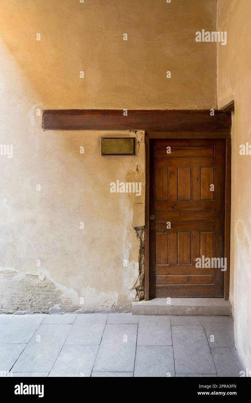 Wooden aged door on grunge stone wall and blank weathered copper door sign Stock Photo